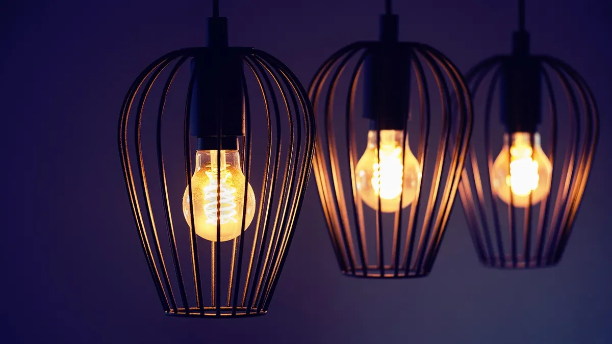 Três luminárias pendentes aramadas com lâmpadas acesas
