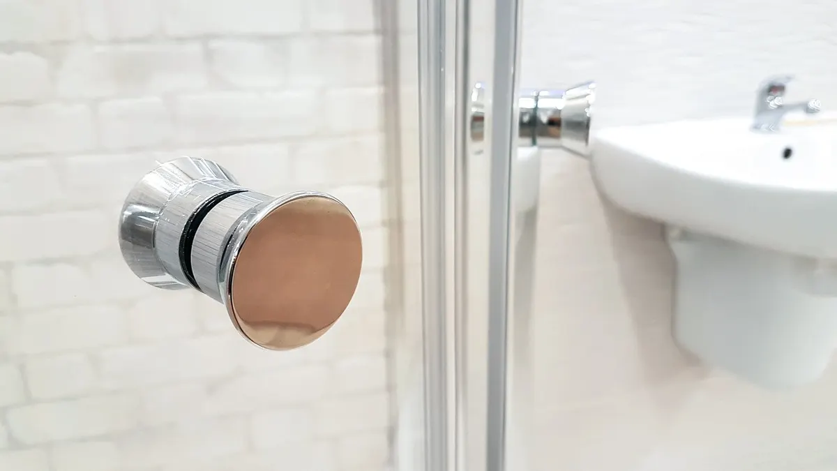 Puxador de porta de box de vidro ao lado de azulejos brancos