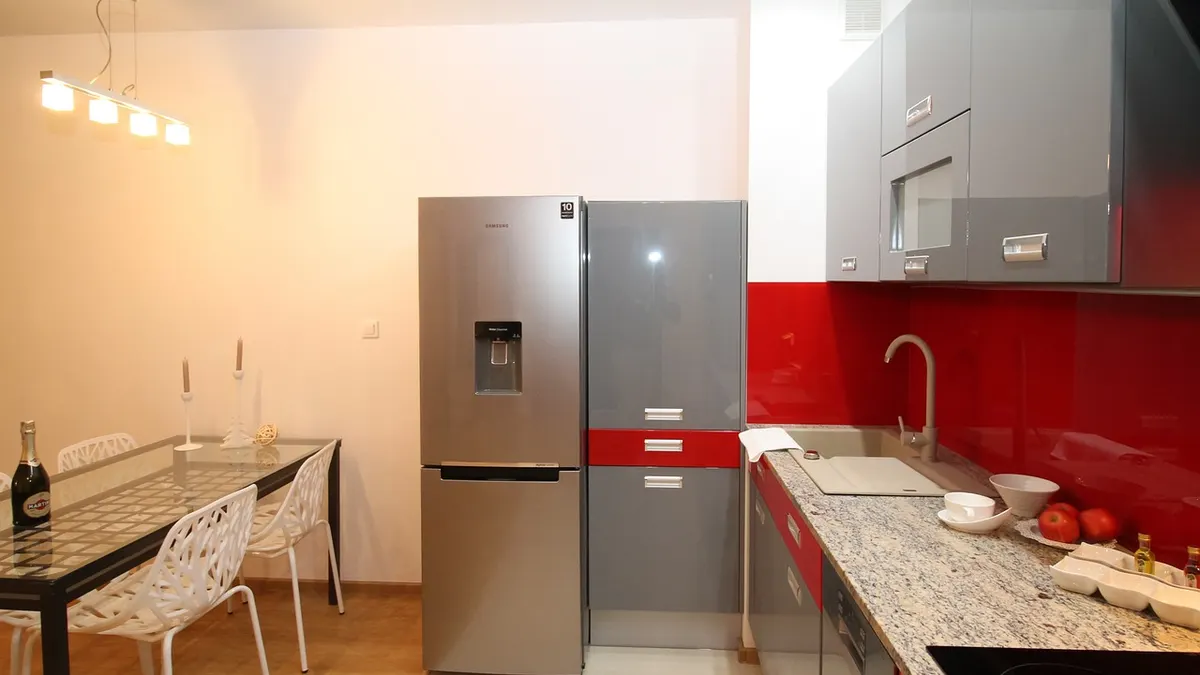 Cozinha com geladeira de inox ao lado de bancada vermelha